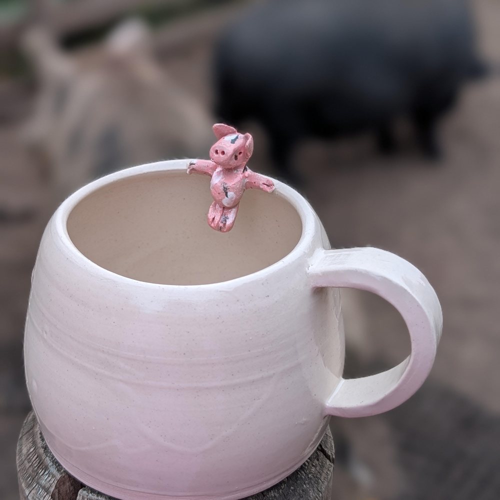 White clay mug with a pink pig perched on the rim