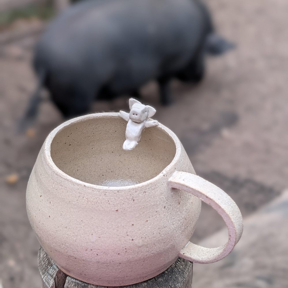 Speckled clay mug with a white pig perched on the rim